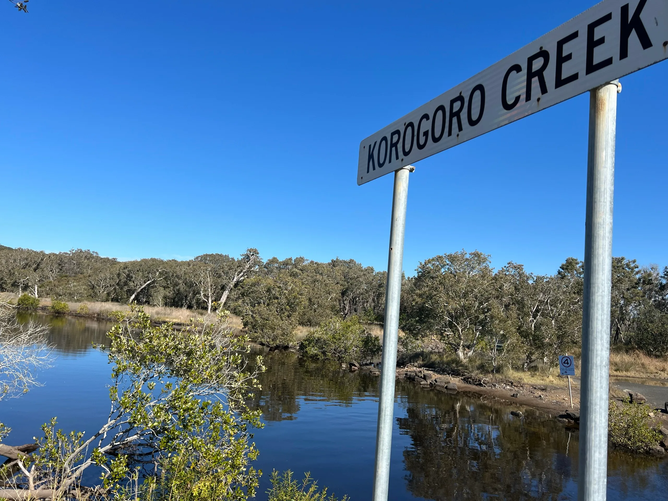 Korogoro Creek name sign beside the calm blue creek at Hat Head