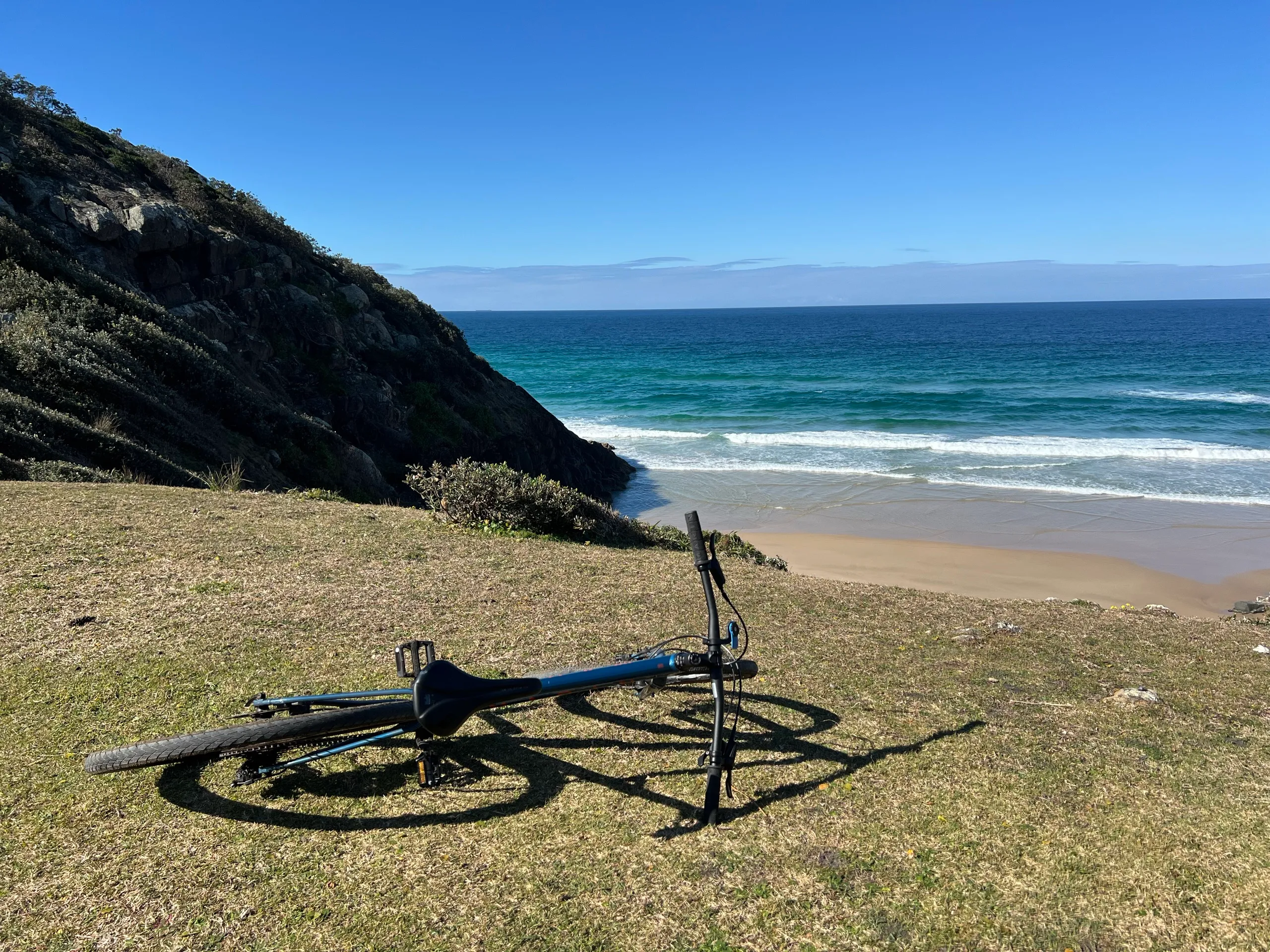 Mountain bike resting on the grassy headland above a turquoise beach at Hat Head