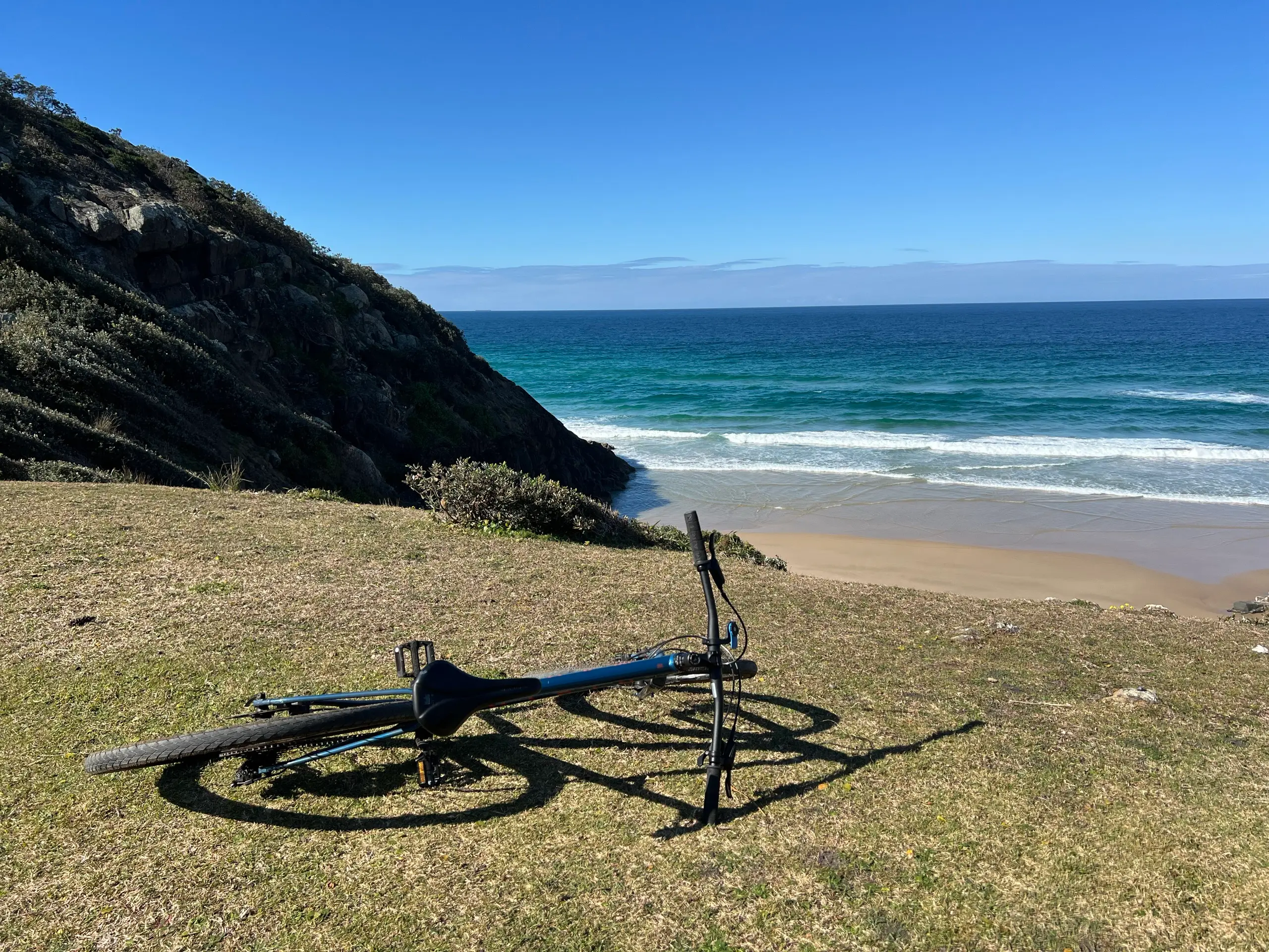 Mountain bike resting on the grassy headland above a turquoise beach at Hat Head