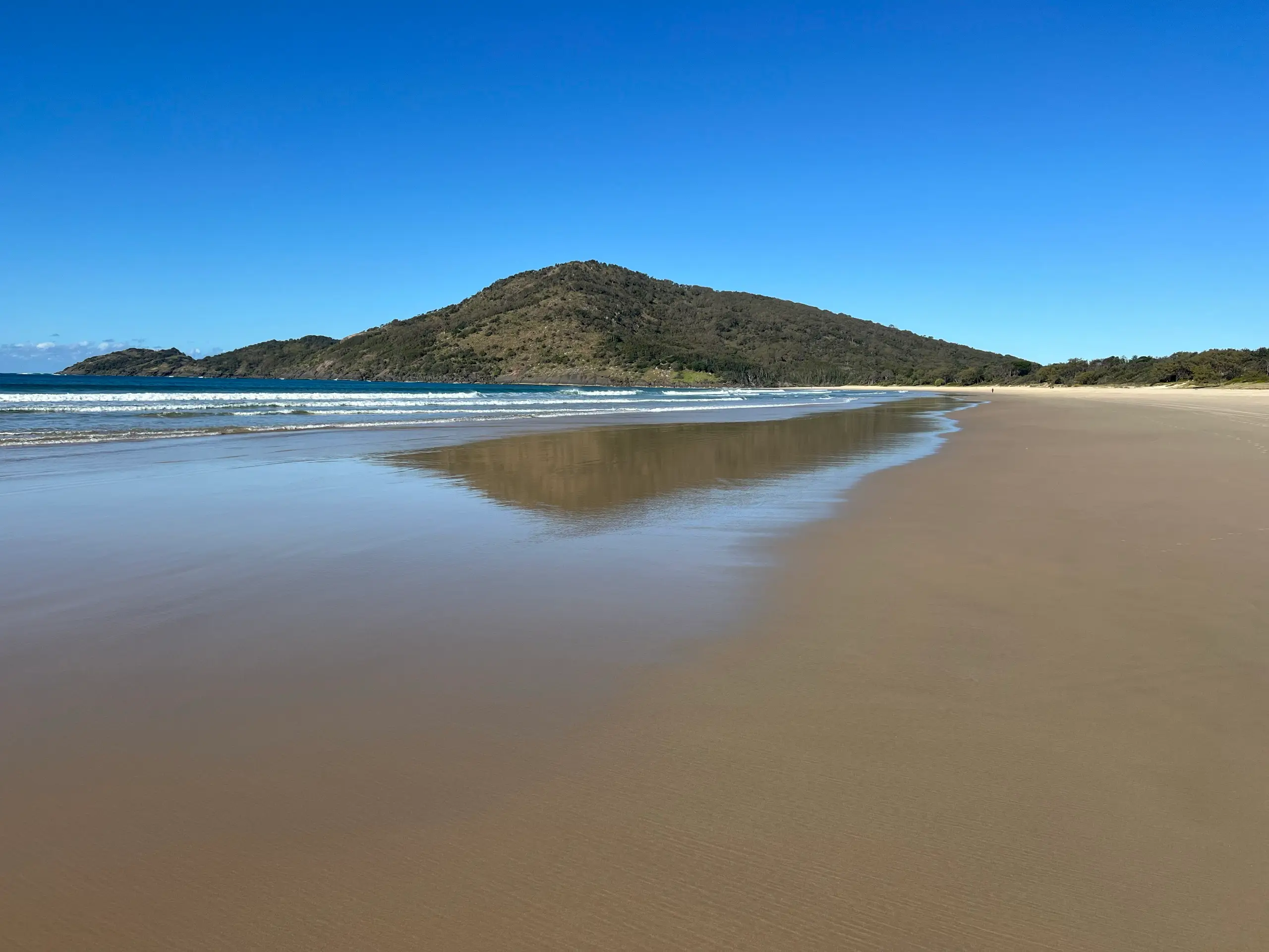 Wide, empty sandy beach at Hat Head with the forested Korogoro headland behind
