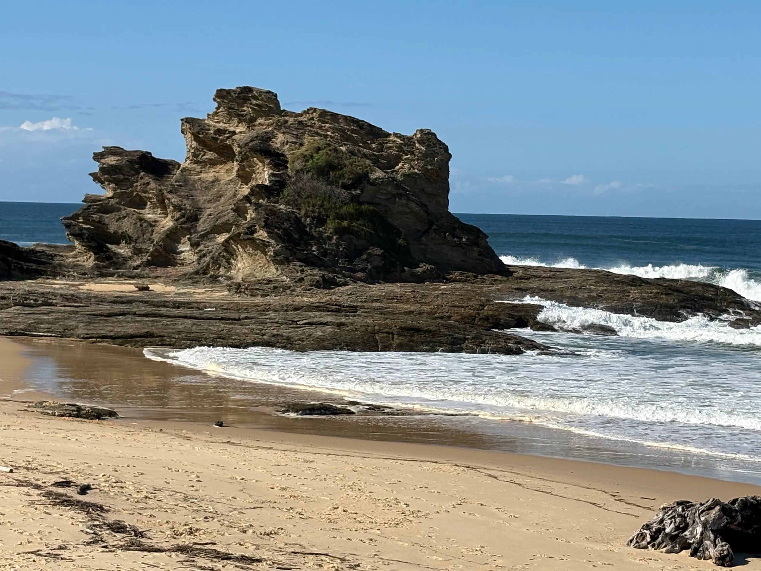 An eroded sea stack on the open beach with surf at Nambucca Heads