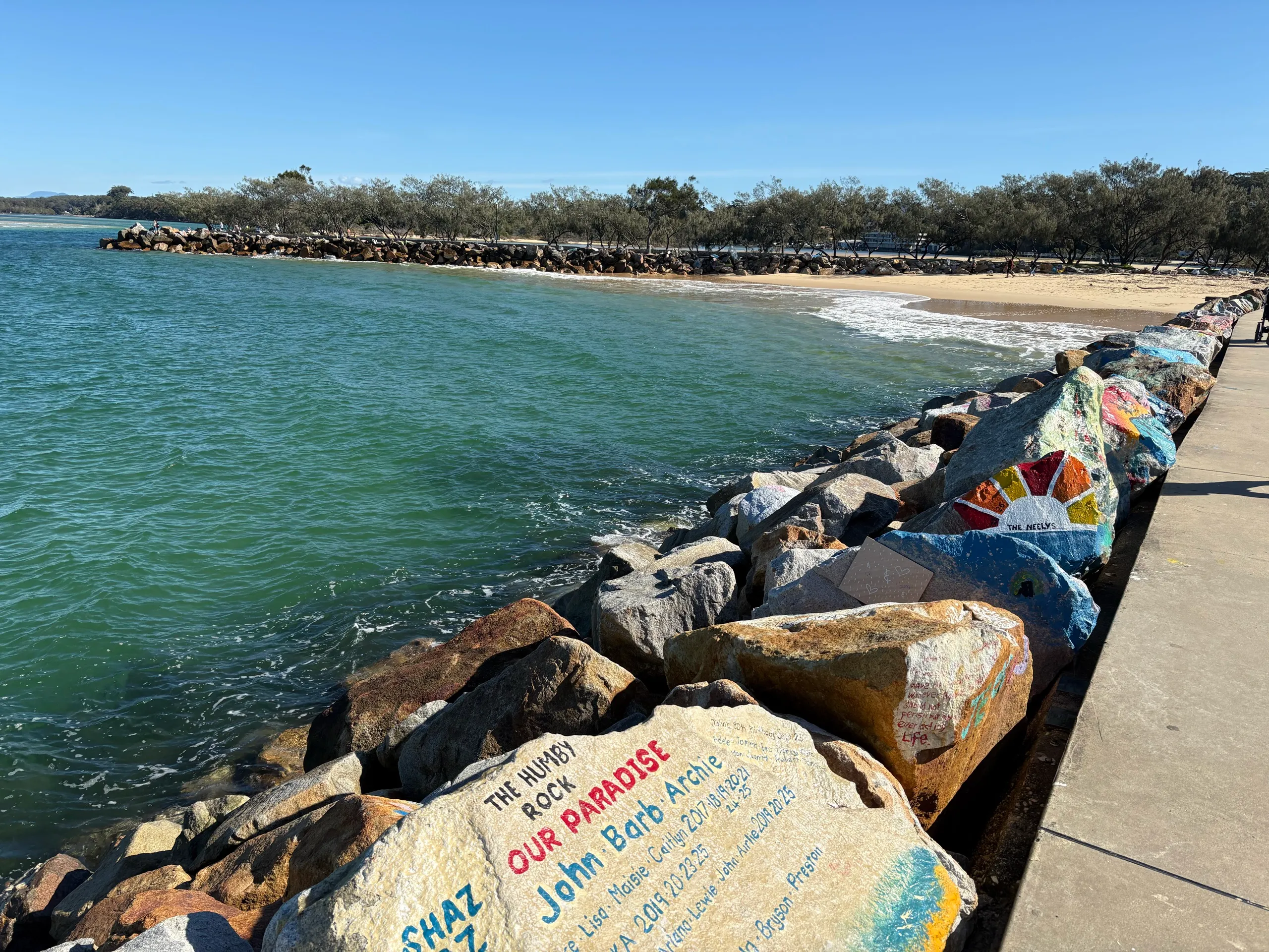 Painted rocks along the V-Wall breakwall with Shelly Beach behind at Nambucca Heads