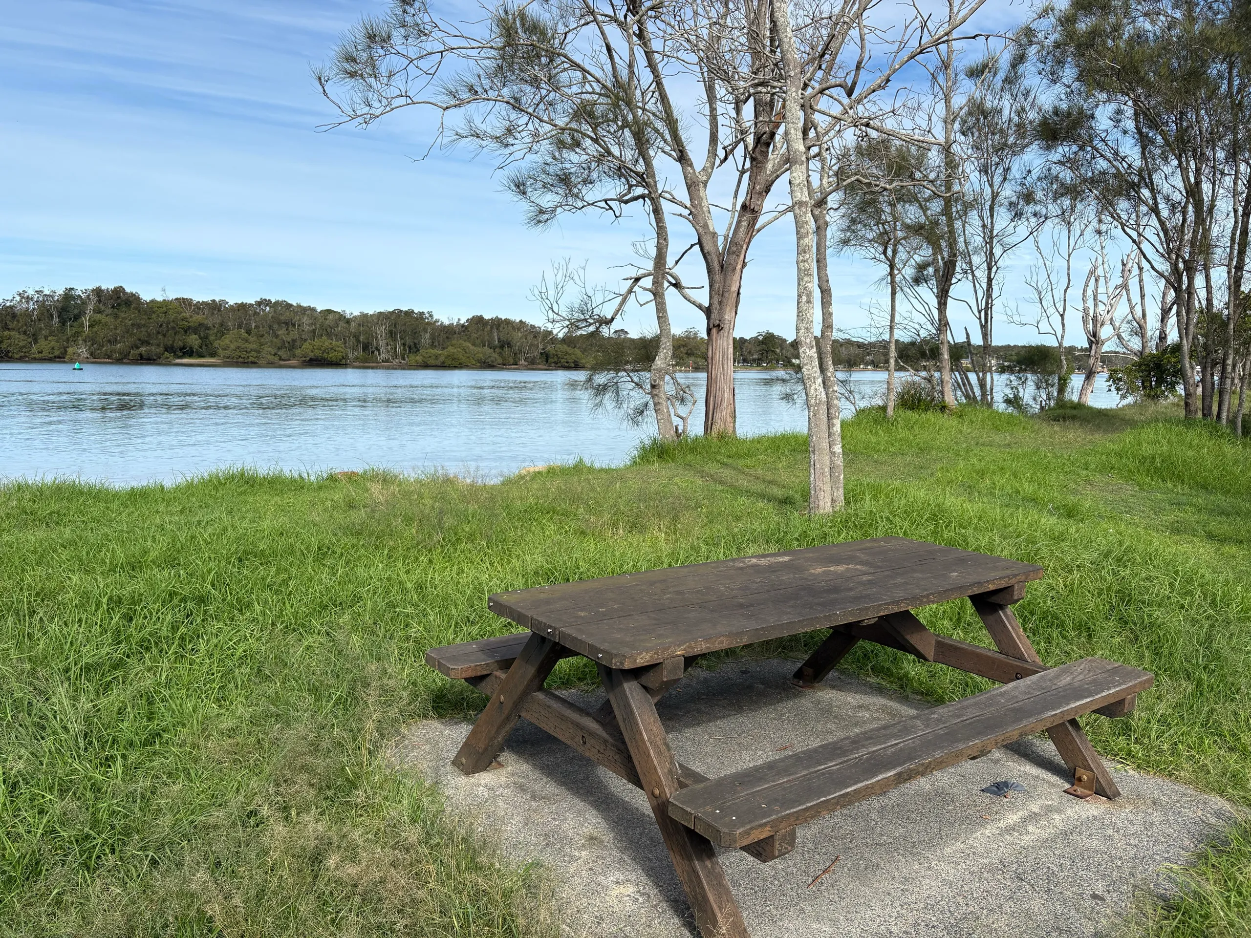 A picnic table on a grassy riverside reserve with moored boats at North Haven