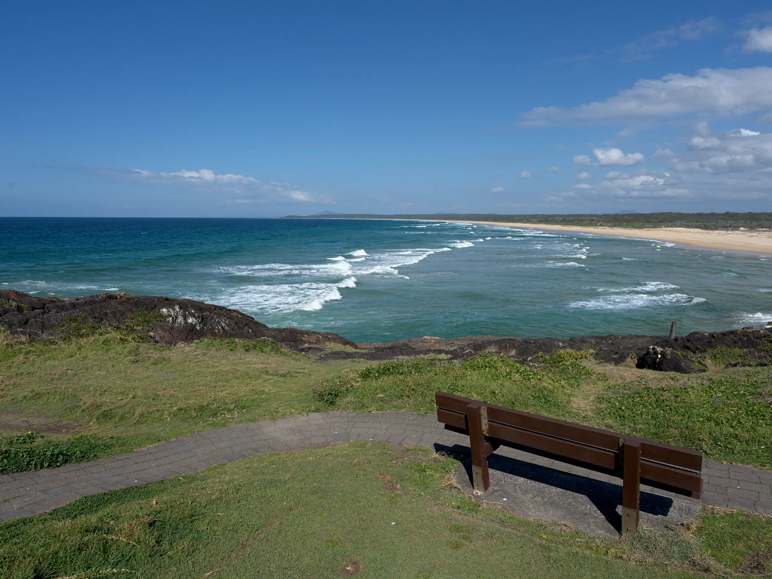A bench on Bonville Headland looking south along the empty sand of Bonville Beach