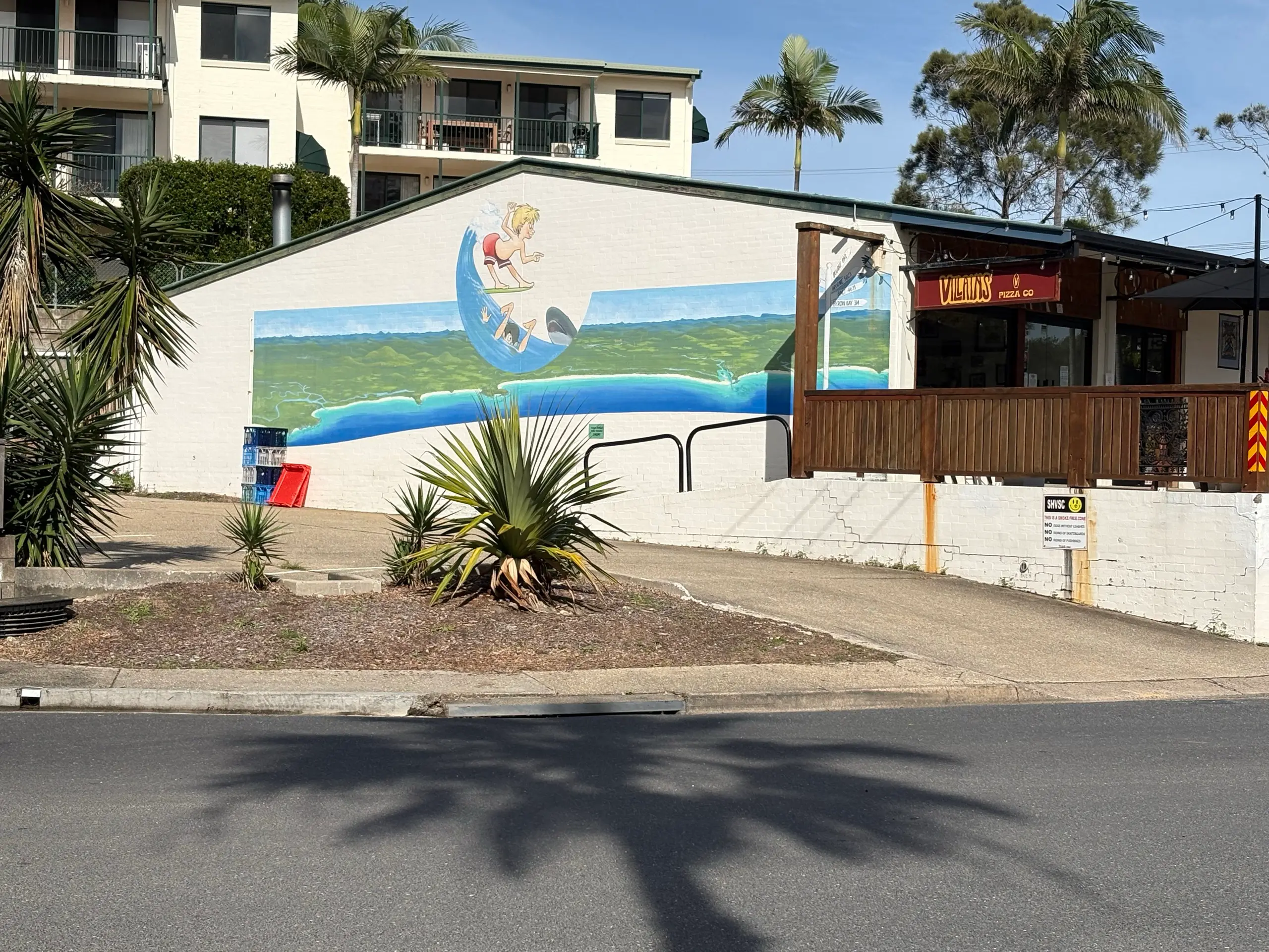 A painted surfing mural on the side of a building in the Scotts Head village, with palms and a cafe