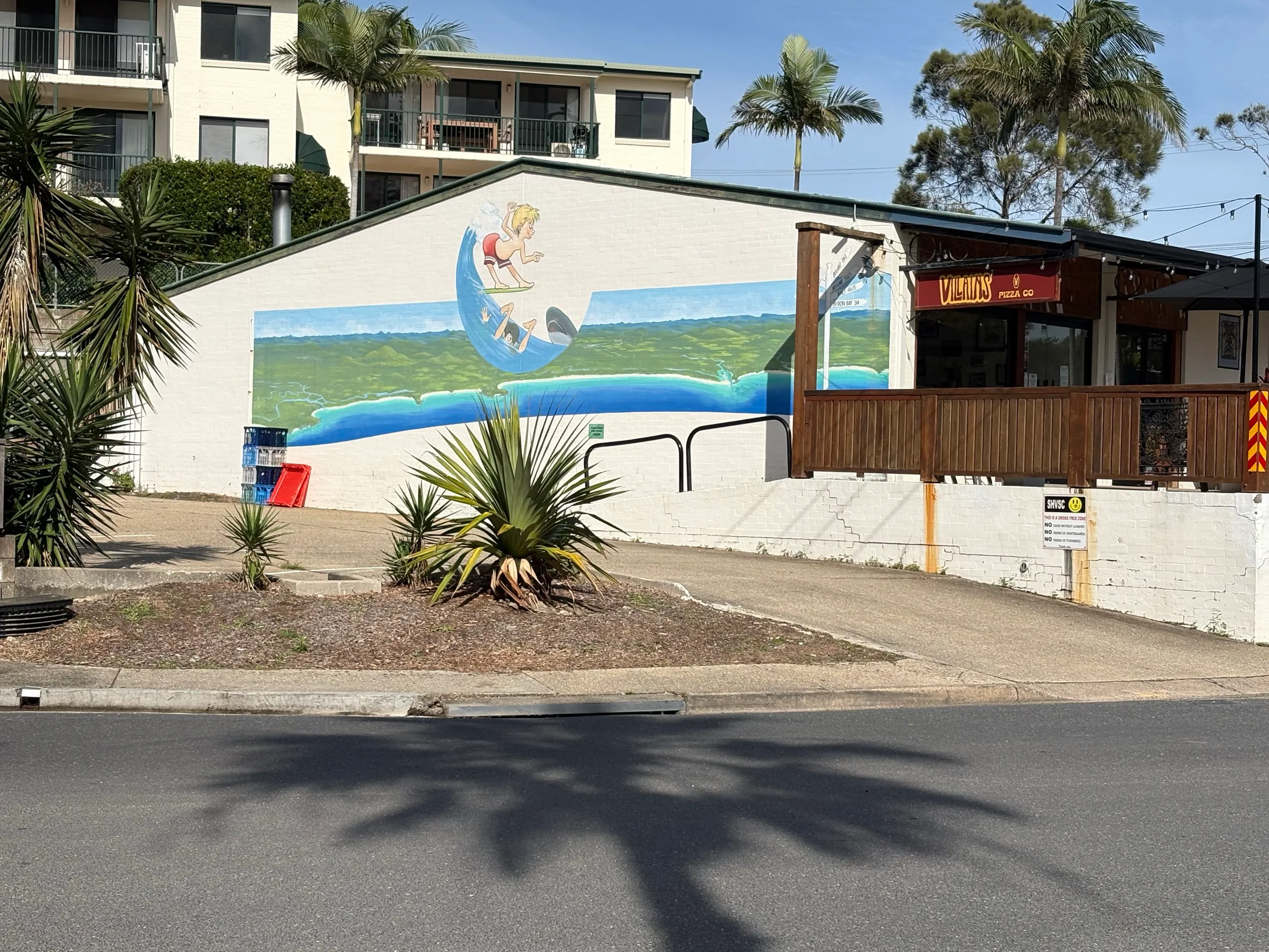 A painted surfing mural on the side of a building in the Scotts Head village, with palms and a cafe