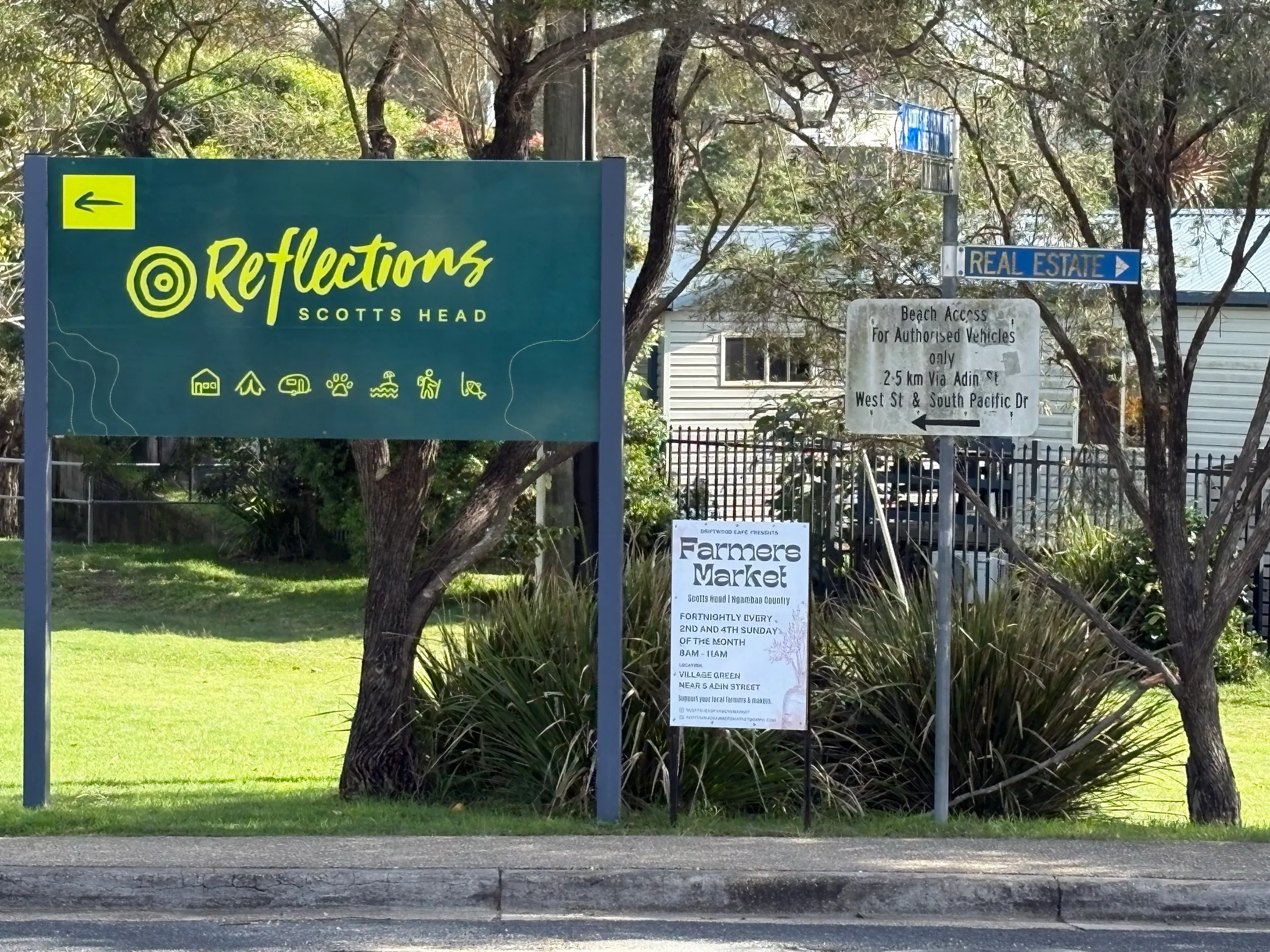 The entrance sign to Reflections Scotts Head Holiday Park beside a farmers market notice