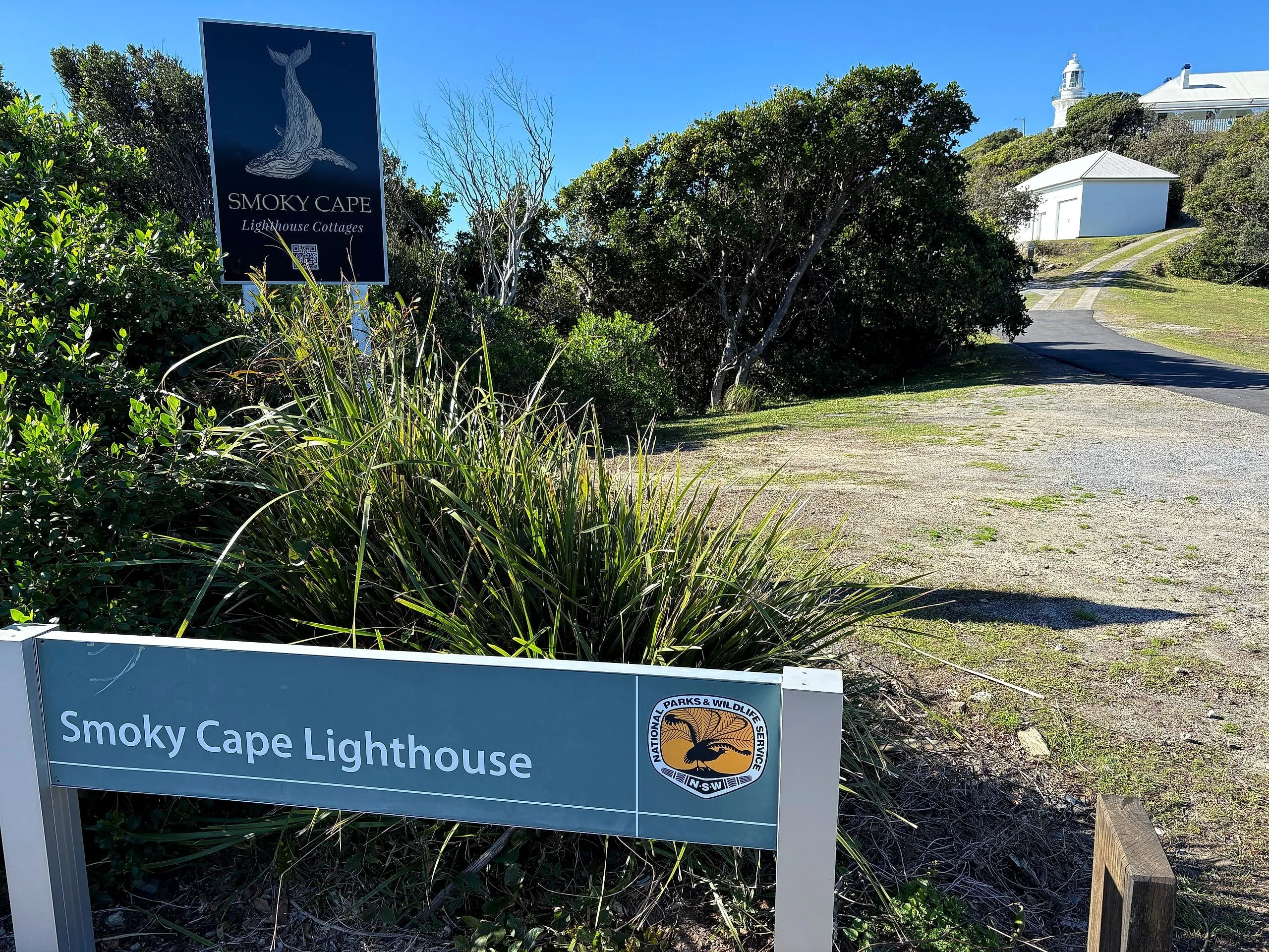 Smoky Cape Lighthouse entrance signs, with the tower just visible above the trees