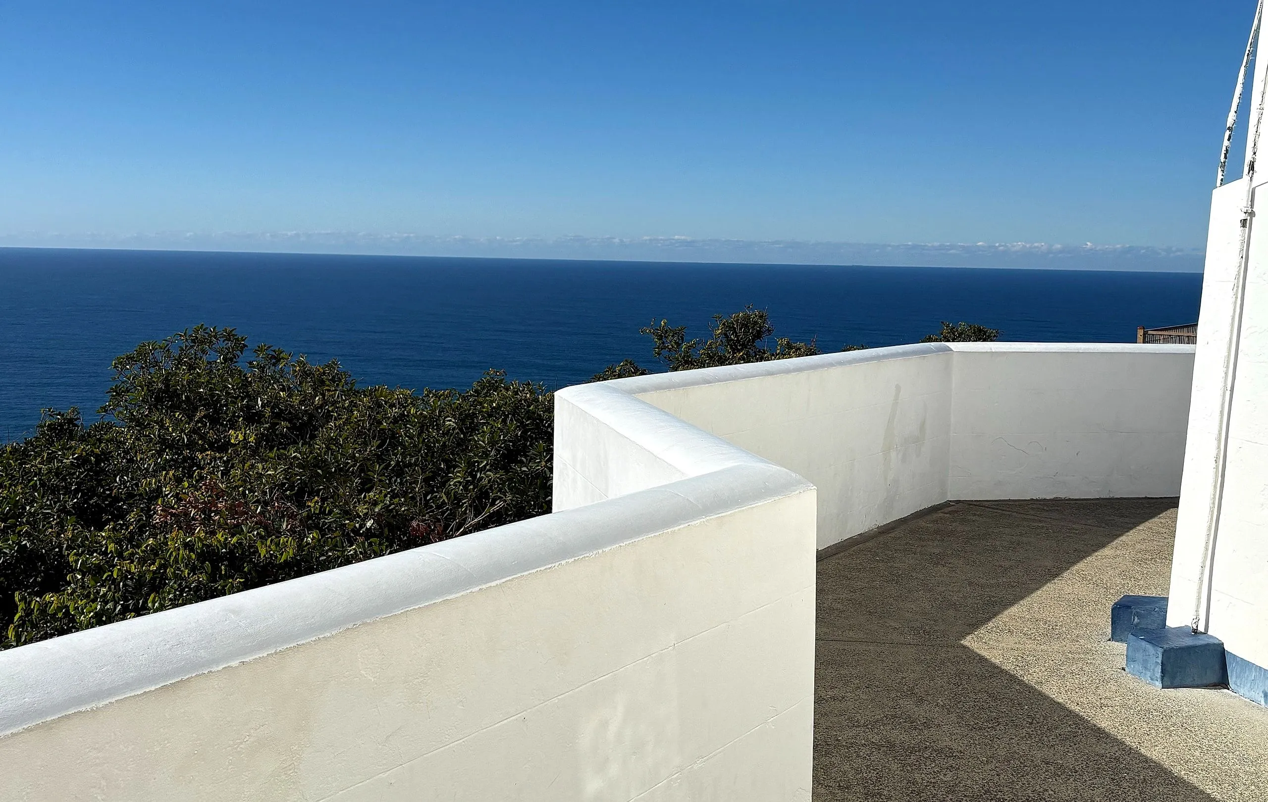 The white parapet wall around the lighthouse terrace with the Pacific horizon beyond
