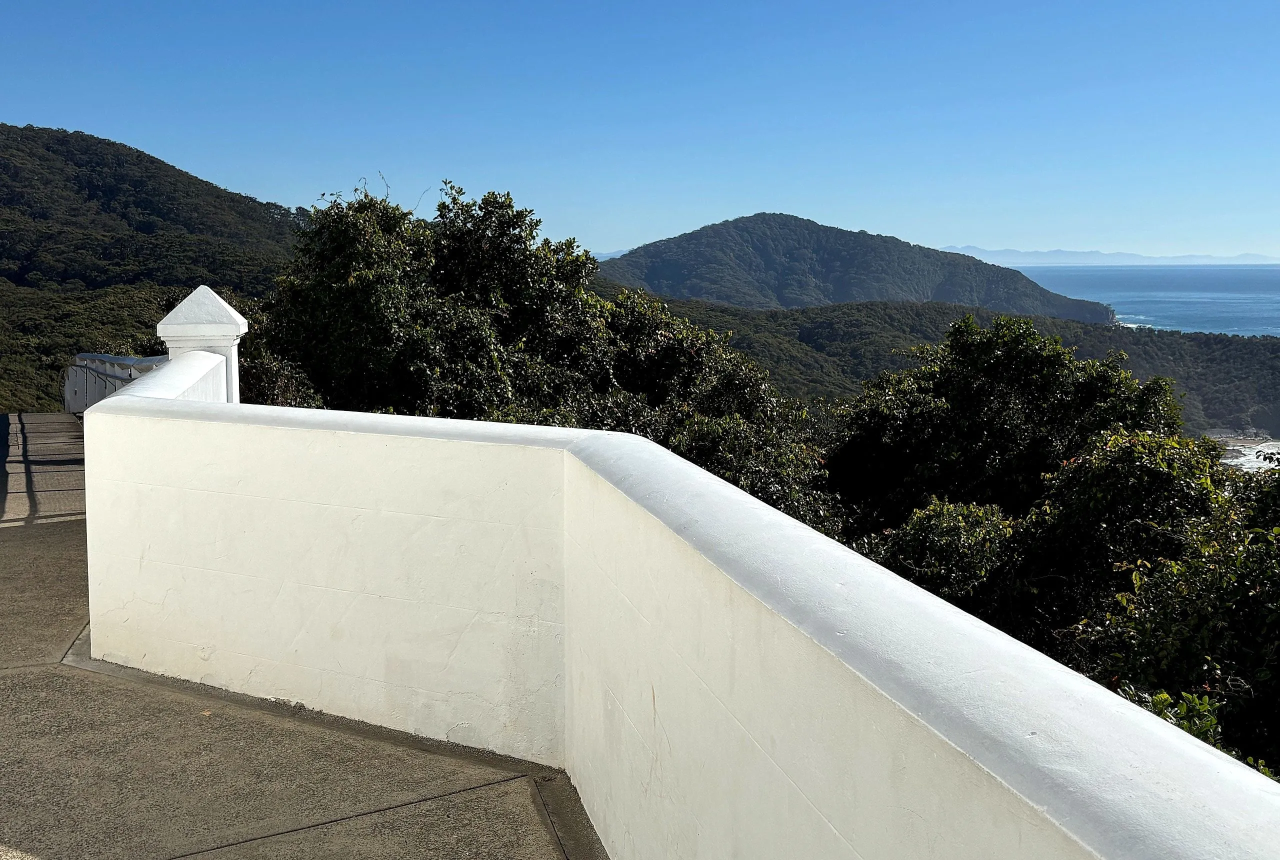 The curved white wall of the lighthouse terrace with forested ranges behind