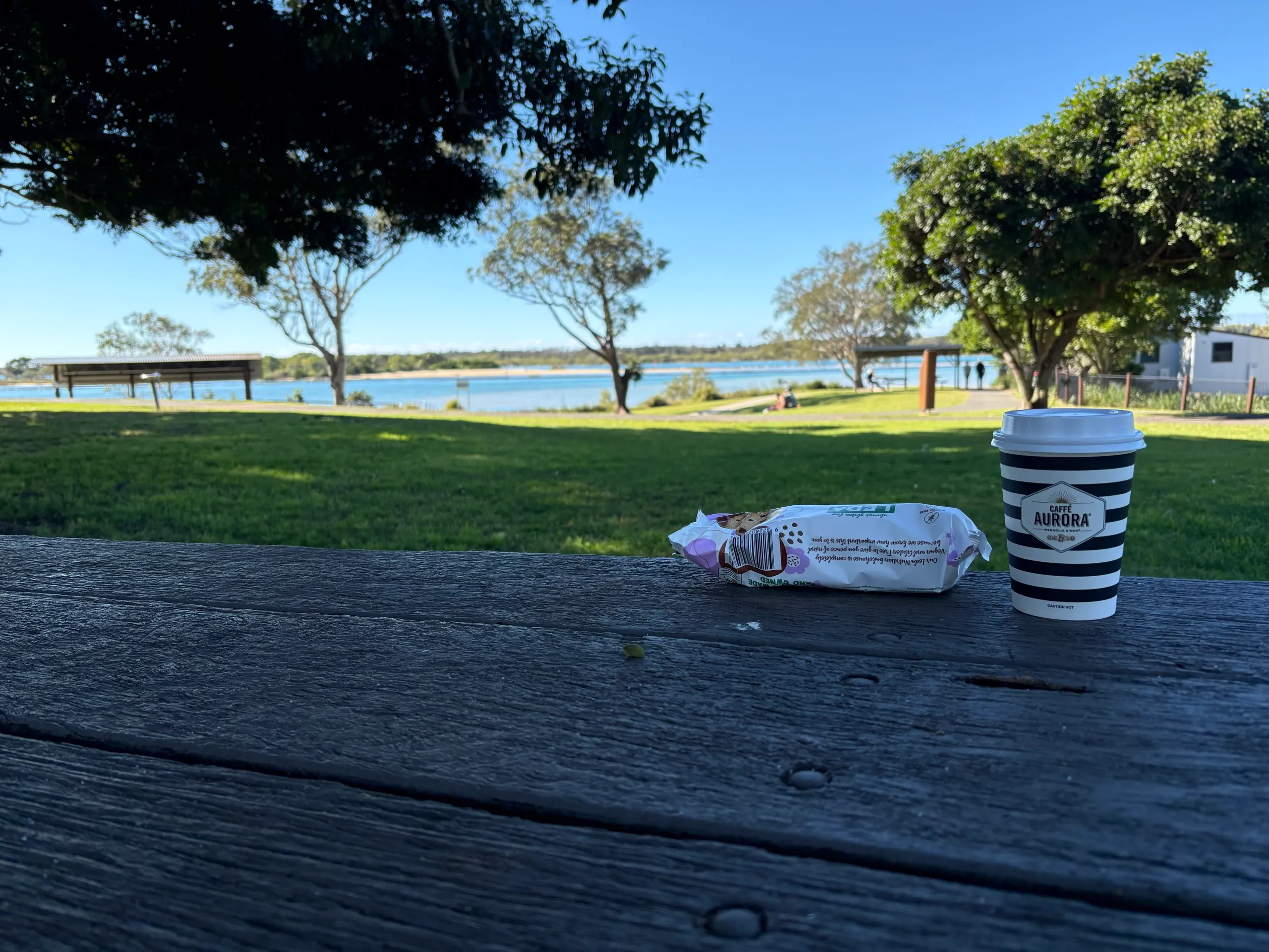 A takeaway coffee on a picnic table by the Urunga riverfront park and lagoon