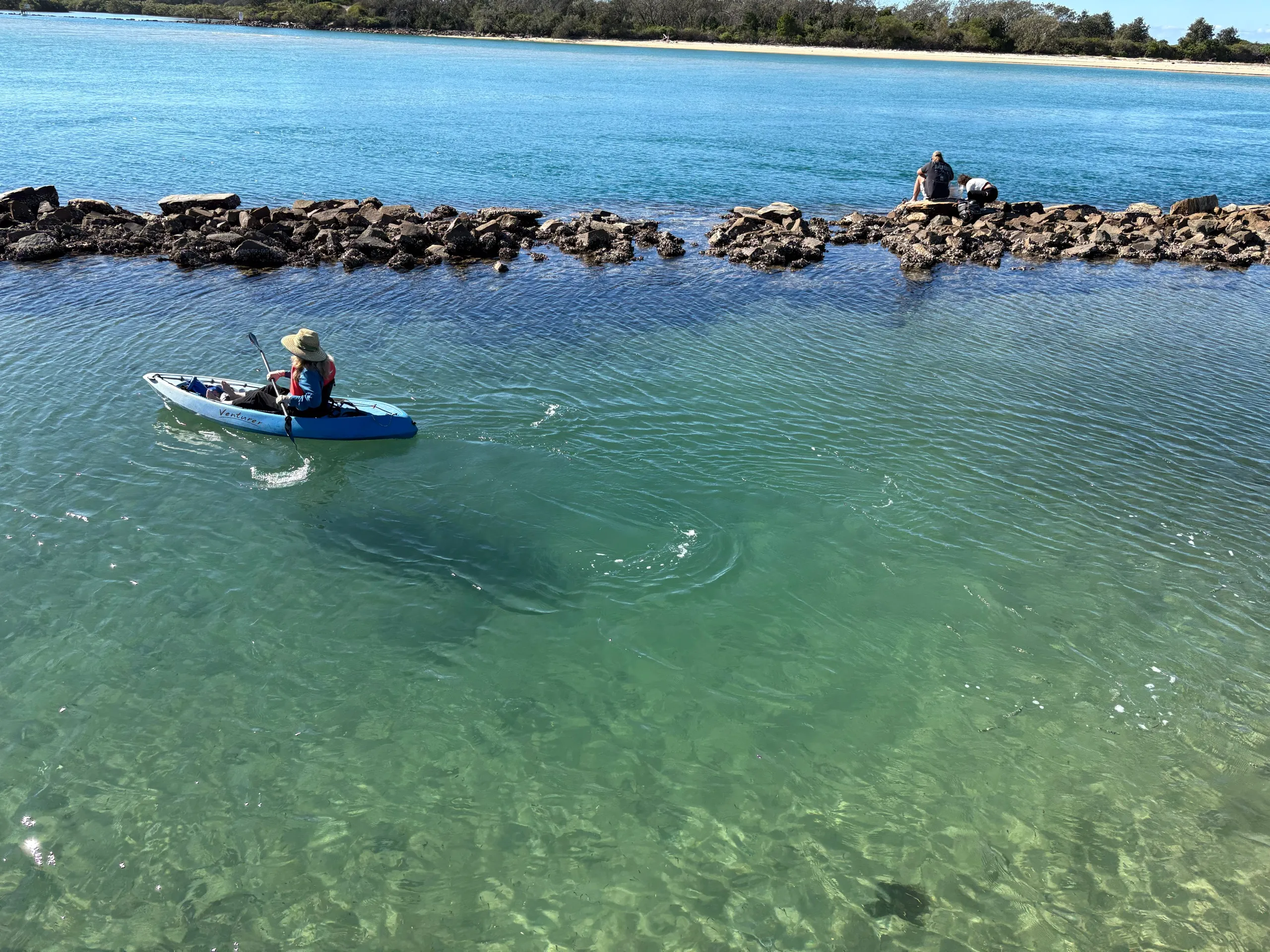 A kayaker in the clear green water of the Urunga river mouth beside the breakwall