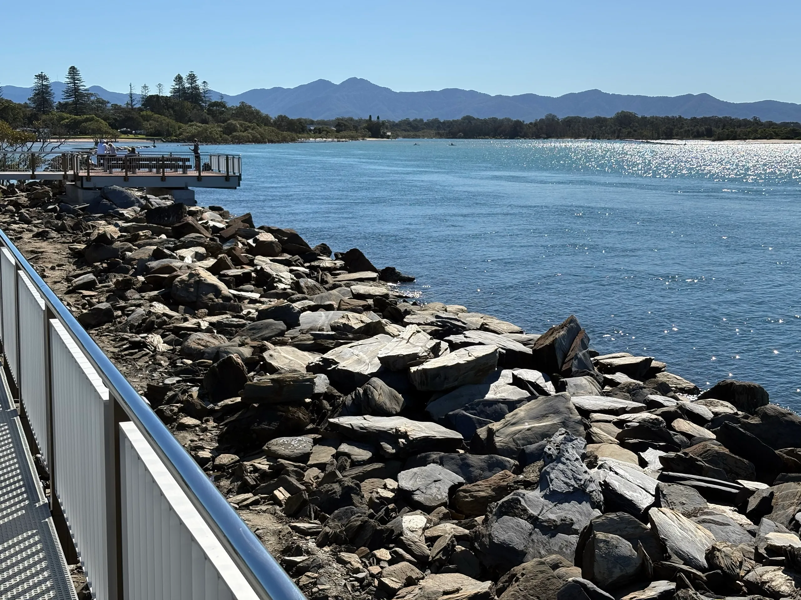 The rock breakwall and river mouth at the end of the Urunga Boardwalk, with mountains in the distance
