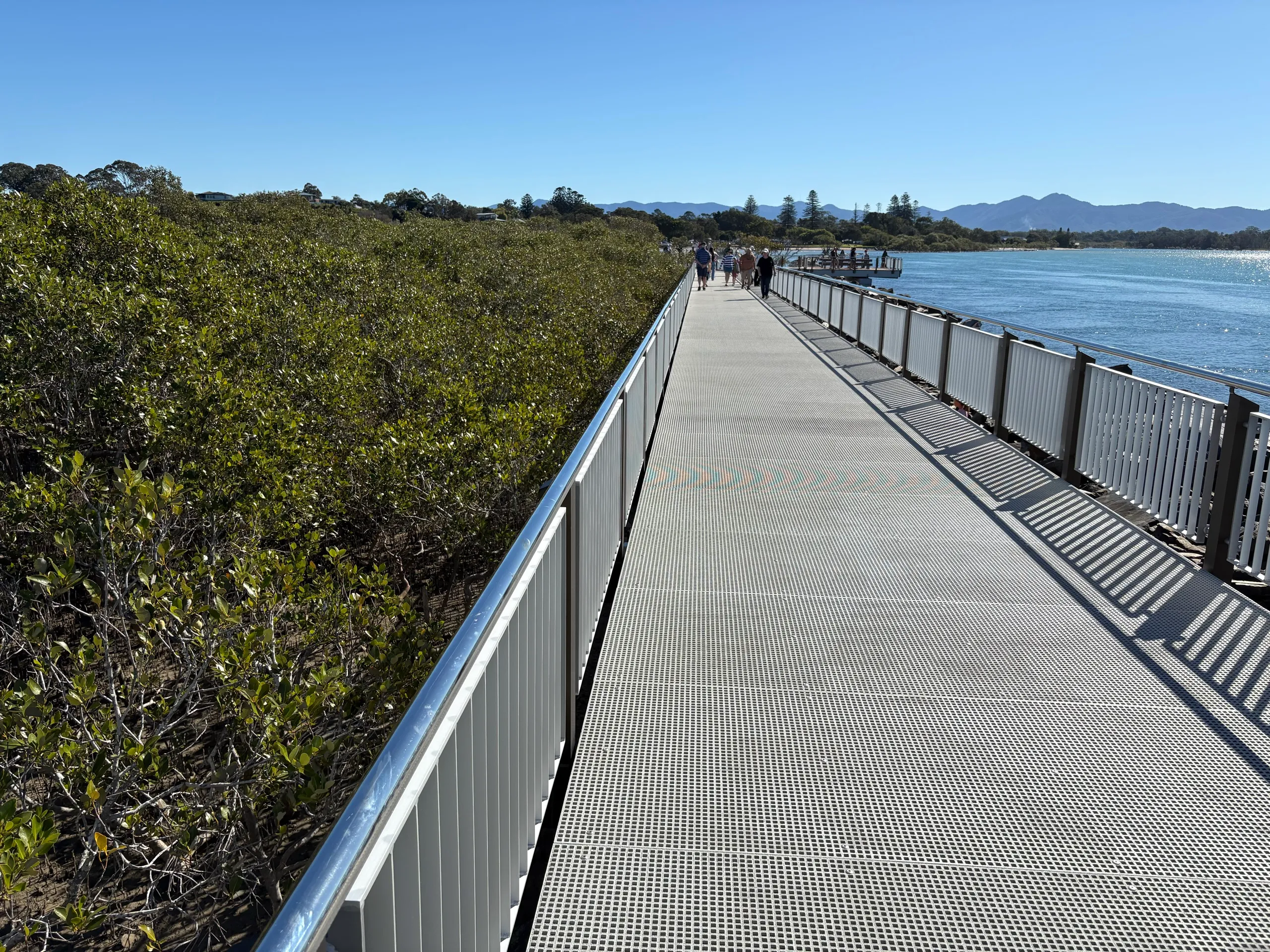 The long metal Urunga Boardwalk leading across the estuary toward the hills
