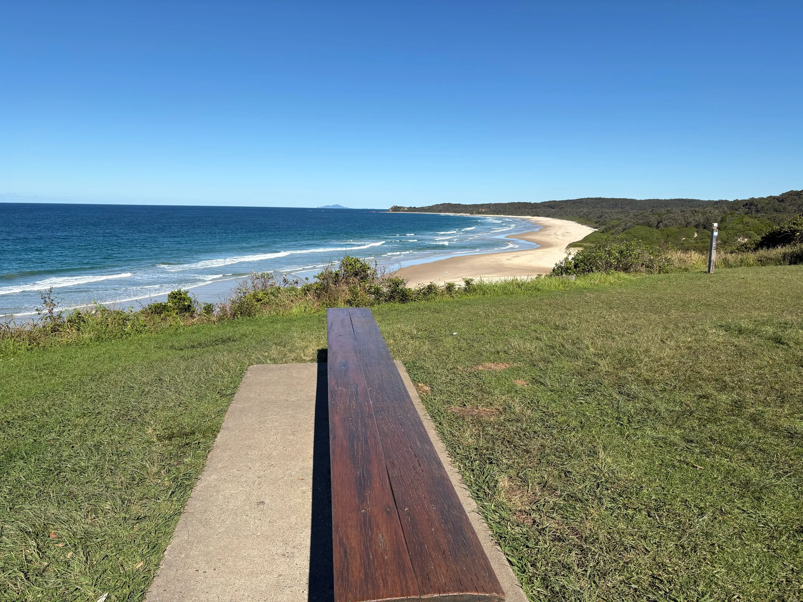 A bench on the grassy headland above a long empty beach near Urunga